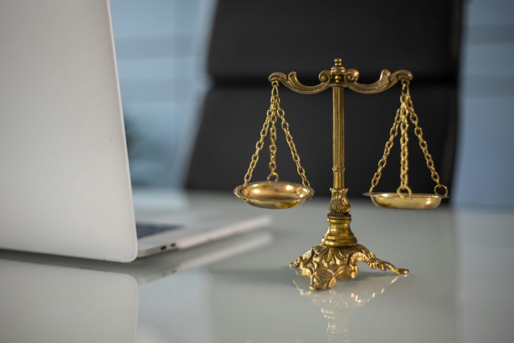 Sprawy karne – Co warto wiedzieć? Golden justice scales on a desk beside a laptop, symbolizing law and balance.