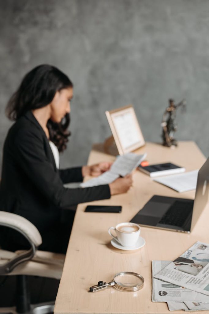 Asian woman in office attentively reading paperwork at a desk.